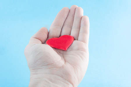 on the outstretched palm lies a red heart. blue background.