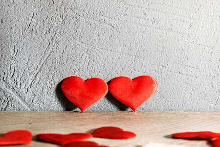 two red hearts stand next to a wooden table against a textured wall. other hearts are scattered...