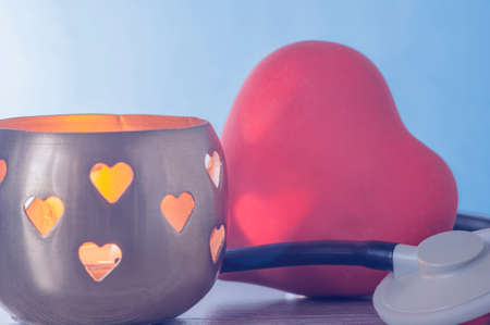 A red heart next to the candle holder in which the candle is burning. The candlestick has holes in...