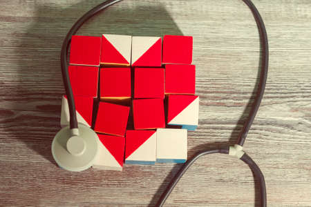 a mosaic of cubes in the form of an unhealthy red heart that carefully encircles a medical statoscope. concept of medicine, care.の写真素材