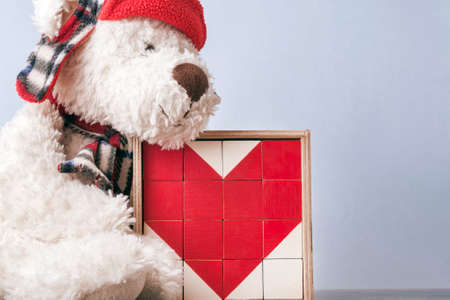 white teddy bear in a red hat with a heart. the heart is laid out with a mosaic of cubes. holiday...