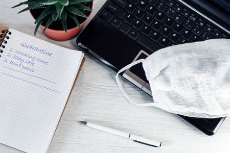 The concept of working during quarantine. On a wooden table, an open notebook with notes, a laptop, a gauze bandage, and a pen.の写真素材