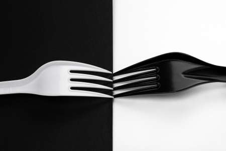Two plastic forks lie with their teeth facing each other. There is a white fork on a black background, and a black one on a white one.の写真素材