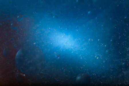 Drops of vegetable oil in water on a blue background. The drops resemble planets and stars.