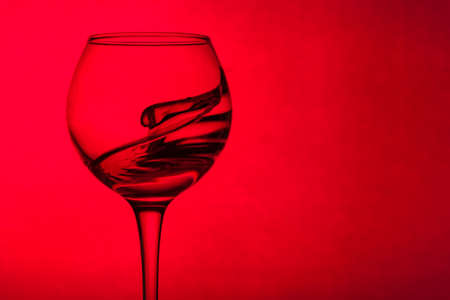 Wine glass with liquid on a red background. The liquid in the glass splashes. Copy spaceの写真素材