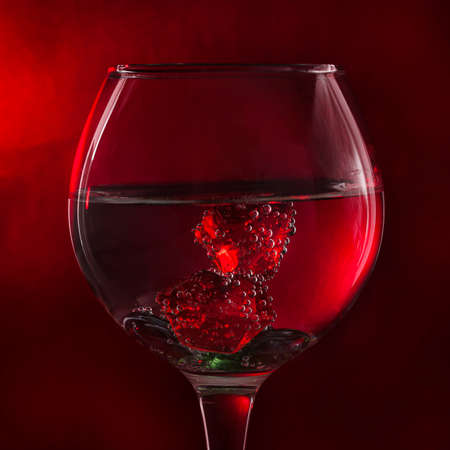 A glass of liquid on a red background with red pieces of ice. The pieces are covered with air bubbles. Backgrounds and textures.の写真素材