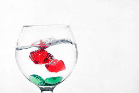 A glass of liquid on a light background with red pieces of ice. The pieces are covered with air bubbles. Backgrounds and textures.の写真素材