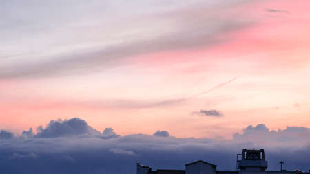 Sunset sky over the city. On the slightly visible roofs of houses thick dark clouds, above the...
