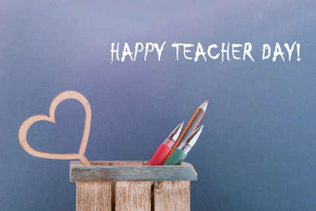 Teacher's day greeting card. In a wooden box pens, pencils heart. Blue background.