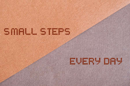 On a textured brown background divided by a diagonal quote small steps every day. Motivational...