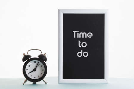 In a black-and-white frame, the inscription time to do. Next to the frame is a vintage alarm clock.の写真素材