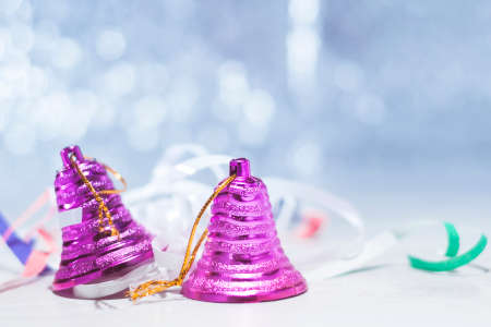 Two pink Christmas bells on a table with festive tinsel on   blue bokehの写真素材