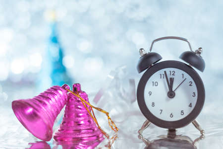 Two pink Christmas bells and a clock on a table with festive tinsel on  blue bokeh