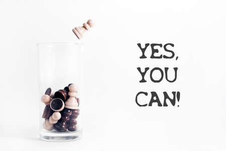 Motivational quote Yes, you can.On a white background-a glass Cup filled with chess pieces. The...
