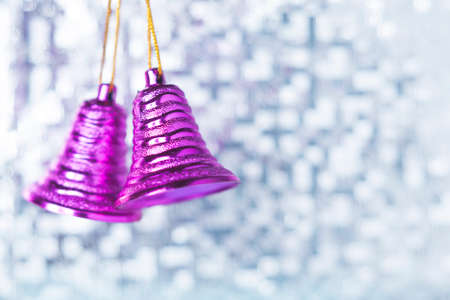 Two purple Christmas bells hang against a blue bokeh background. Selective focus.