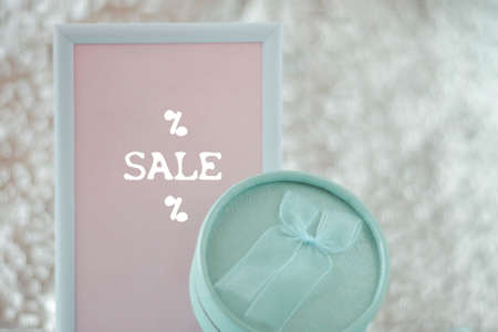 Round light green gift box next to a white and pink frame with the inscription sale. The background...