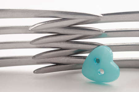 Closeup of the crossed tines of two forks. Next to it is a blue button in the shape of a heart....