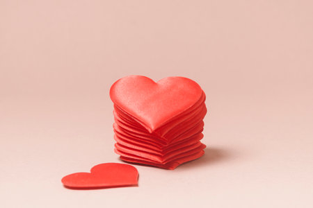 A stack of hearts on a pink background. Next to it lies a separate heart.の写真素材
