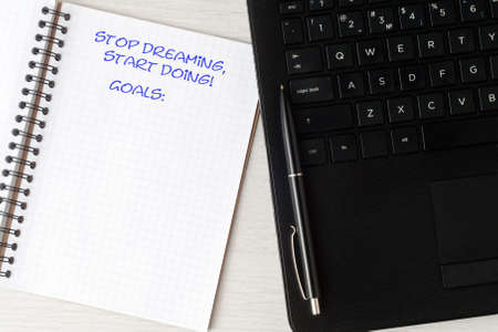 On the table is a laptop and an open notebook. The inscription in the notebook "Stop dreaming, start doing". Just below the label is the goal.の写真素材