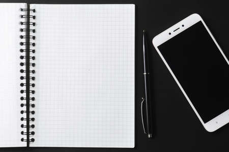 An open notebook, a black pen, and a white smartphone on a dark background.