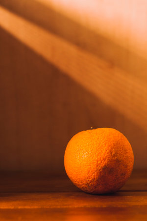 Still life with an orange. An orange on a wooden table. There are slanting beams of light on the wallの写真素材