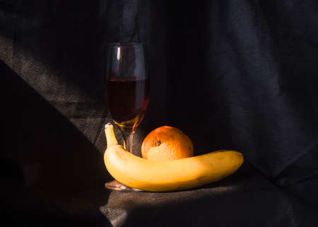Still life with a banana, orange and a glass of red wine on a dark background.の写真素材