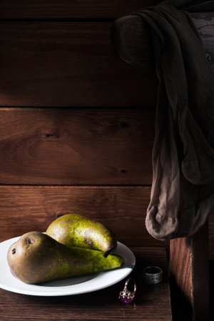 Still life with two pears on a white plate. Next to it are two rings. A woman's nylon stockings hang from the back of a chair.の写真素材