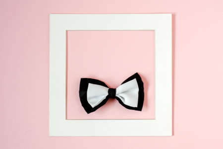 Black and white bow tie in a square white frame. Pink background. Copy space.