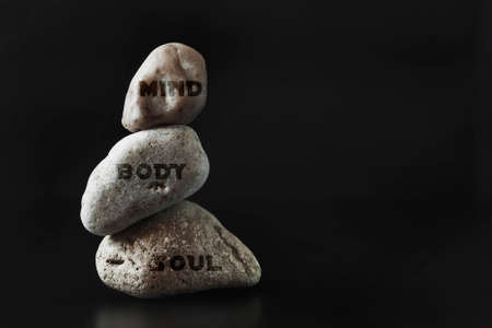 Three stones stand on top of each other keeping their balance. Dark background. Copy space ..の写真素材