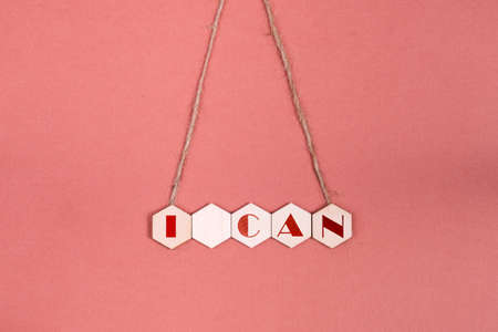 Motivational quote I can. On a pink background, five wooden hexagons with an inscription hang on a rope.の写真素材