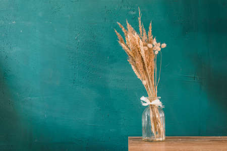In a glass bottle, a bouquet of dried herbs stands on a wooden table against a dark green textured wall. Copy space.の写真素材