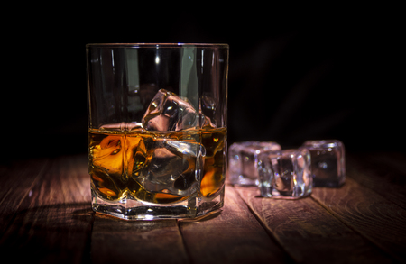 A glass of whisky and some ice cubes on the wooden tableの写真素材