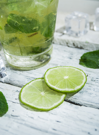Mojito cocktail with slices of lime and mint leaves in highball glass on a wood table. White background.の写真素材