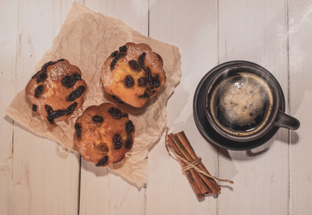 Hot morning coffee, cinnamon sticks and three muffins on wooden backgroundの写真素材