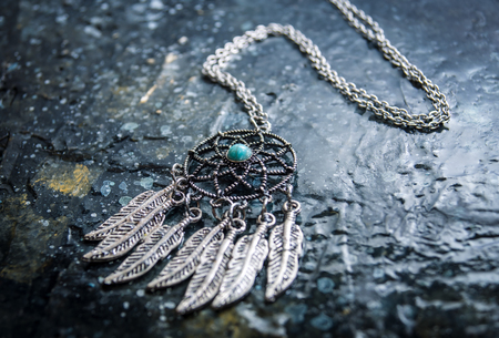 Tiny silver Dream Catcher amulet, an ancient magic talisman on stone backgroundの写真素材