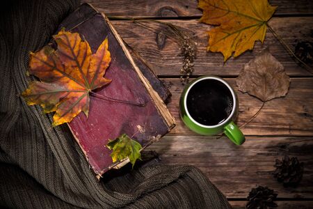 Autumn still life with a cup of coffee, fallen leaves and sweater on wooden backgroundの写真素材