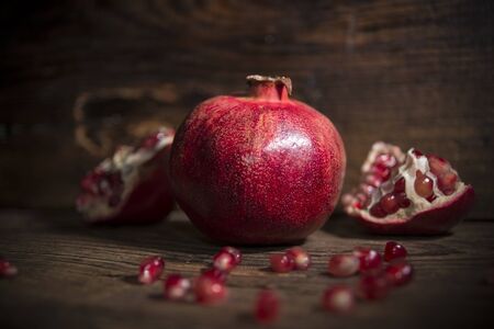 Juicy red pomegranates with aged book on wooden background
