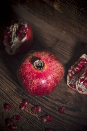 Juicy red pomegranates with aged book on wooden backgroundの写真素材