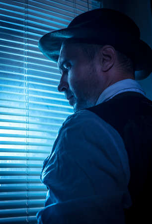Suspicious private detective near the window with blinds, cinematic noir scene
