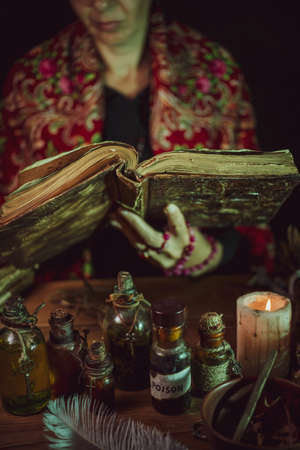 Female witch making potion on dark background, magic bottles with potions and candles on table of alchemist, Halloween themeの素材 [FY310174990486]