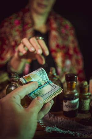 Female witch making potion on dark background, magic bottles with potions and candles on table of alchemist, Halloween themeの写真素材