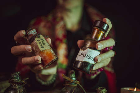 Female witch making potion on dark background, magic bottles with potions and candles on table of alchemist, Halloween themeの写真素材