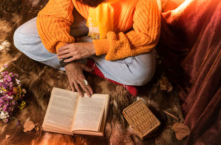 Beautiful woman in orange sweater reading a book and enjoying her coffeeの写真素材