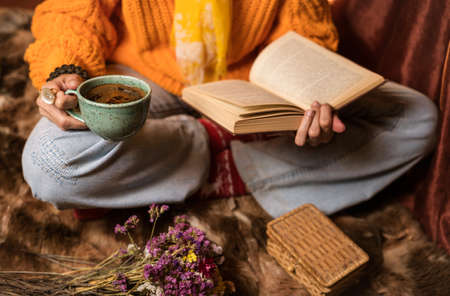 Beautiful woman in orange sweater reading a book and enjoying her coffee