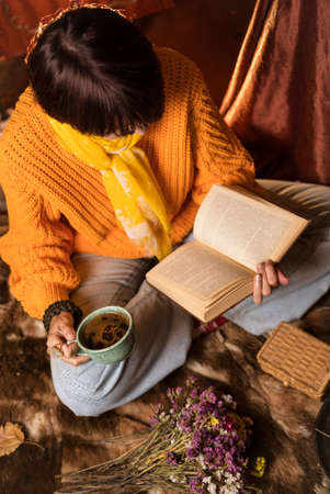 Beautiful woman in orange sweater reading a book and enjoying her coffeeの写真素材