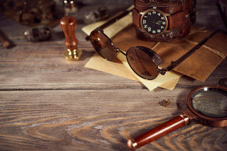 Steampunk still life - old vintage objects on a wooden background. Leather wrist watch, dark glasses, old tube lamps, magnifying glass, gearsの写真素材