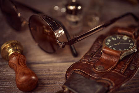 Steampunk still life - old vintage objects on a wooden background. Leather wrist watch, dark glasses, old tube lamps, magnifying glass, gearsの写真素材