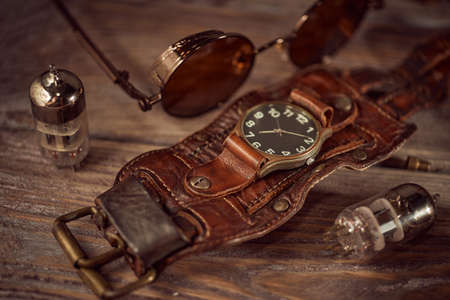 Steampunk still life - old vintage objects on a wooden background. Leather wrist watch, dark...
