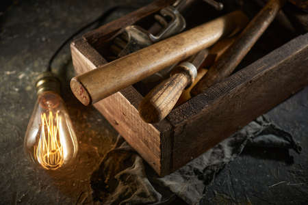 Wooden tool box of used hand tools with old and dirty, rusty wrenches, hammers, and old light bulbの写真素材