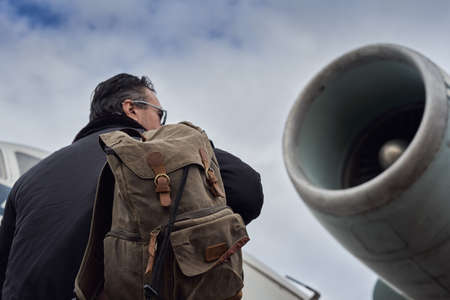Oldschool pilot in the bomber jacket posing near the aircraft, aviator male with scarf and sunglassesの写真素材